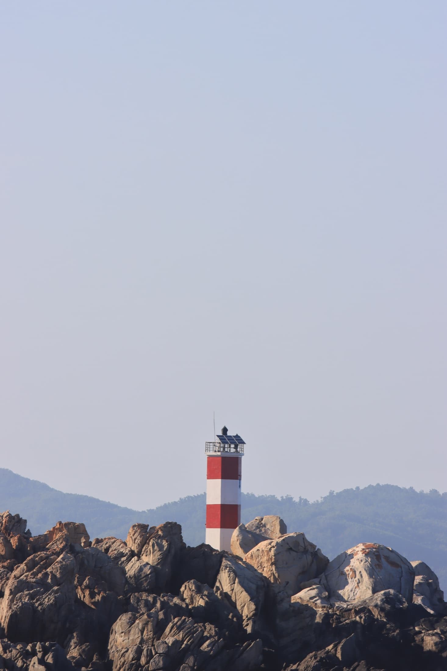 A red and white lighthouse standing among coastal rocks